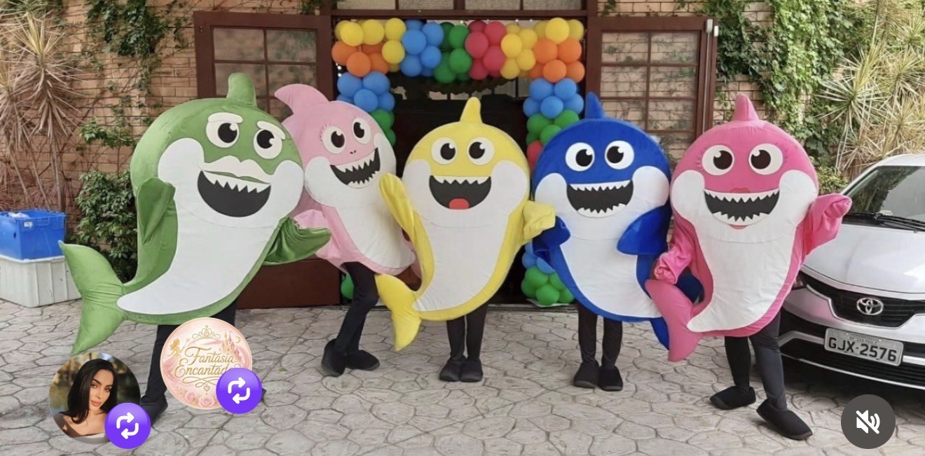 Cinco mascotes coloridos da família tubarão em frente à entrada da festa
