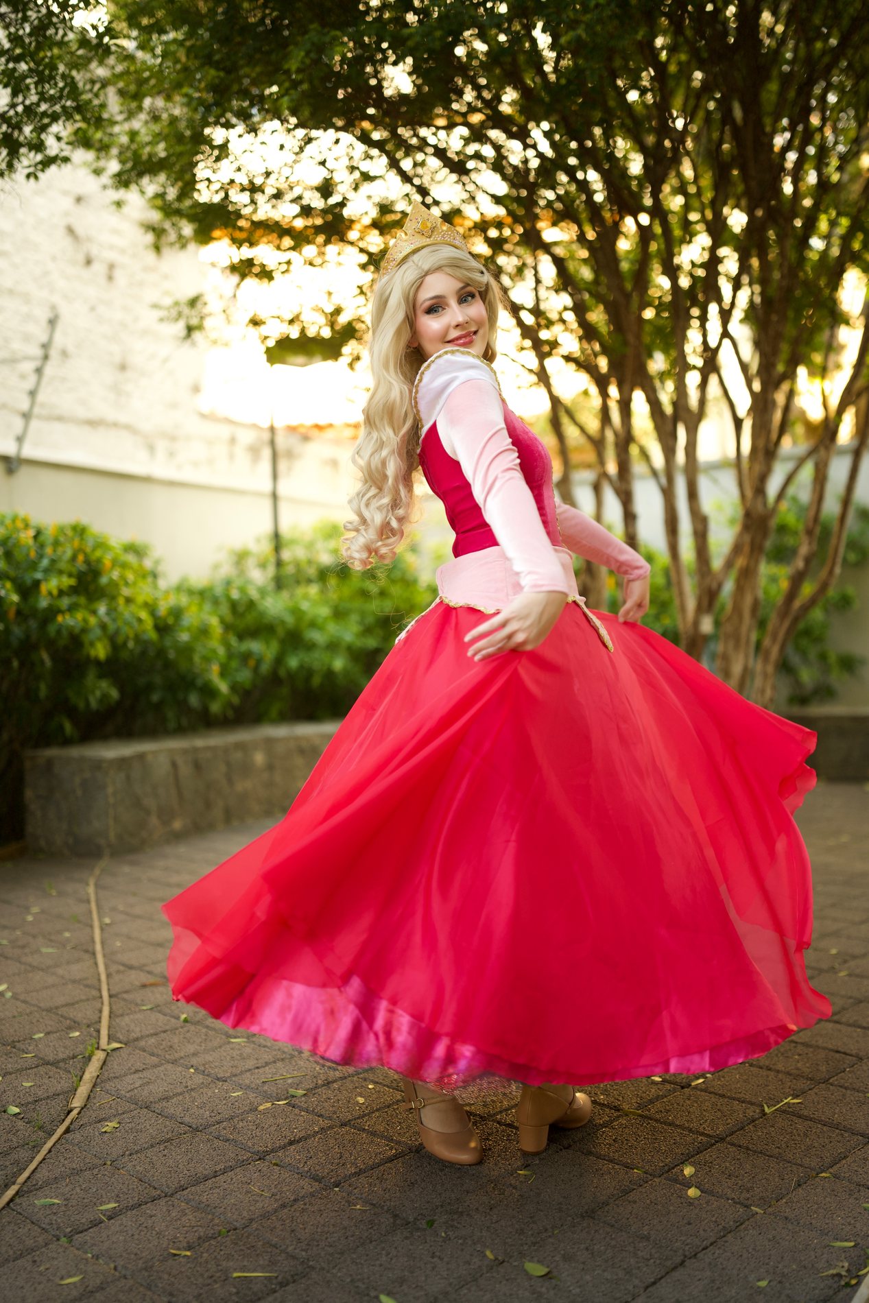 Princesa de vestido rosa e coroa dourada rodando o vestido no jardim ao pôr do sol