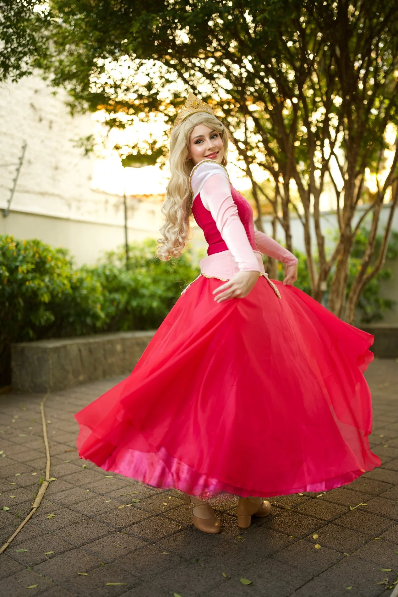 Princesa de vestido rosa e coroa dourada rodando o vestido no jardim ao pôr do sol